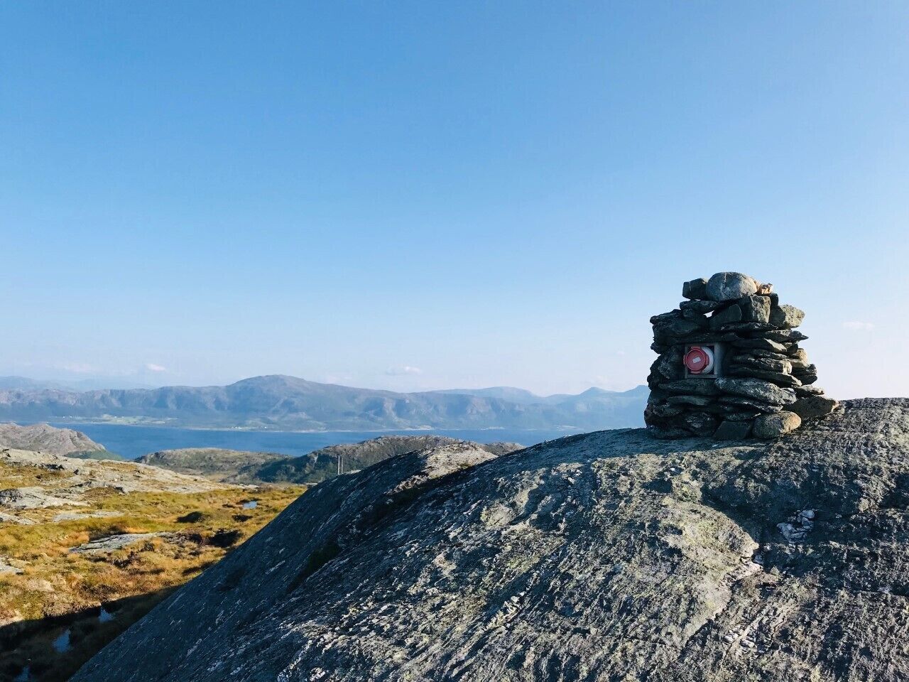 A stone cairn on a rocky outcrop with a clear view of distant mountains and a body of water.