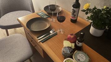 A dining table with a plate, fork, knife, wine glasses, a bottle of wine, an apple, cheese, and a potted plant.