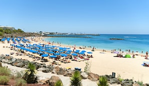A beach with numerous blue umbrellas and sun loungers, rocky terrain, and a clear view of the sea. - Apartment 3 Small block of 6 apartments, a stones through from Marina Rubicon (Yaiza)