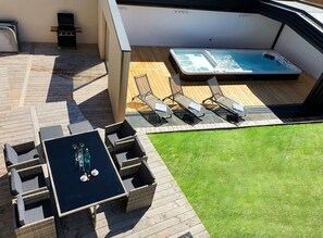 A rooftop patio with a hot tub, lounge chairs, and a table with drinks.