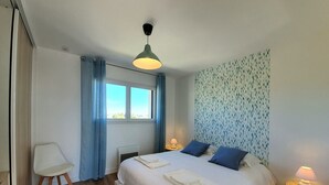 Un dormitorio ordenado con cama, lámparas de noche, una silla y un ventanal con cortinas.