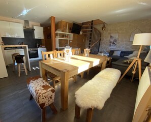 Cocina moderna con armarios de madera, comedor con mesa y sillas de madera, una escalera y una pared de piedra.