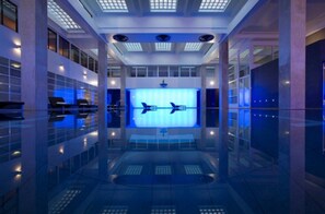Experience the sleek lobby with a high ceiling, central atrium, and reflective floor, featuring seating areas and a large digital display.