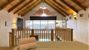 Een ruime slaapkamer met een groot bed, houten balken in het plafond, uitzicht op het landschap en een balkon met een hekwerk.