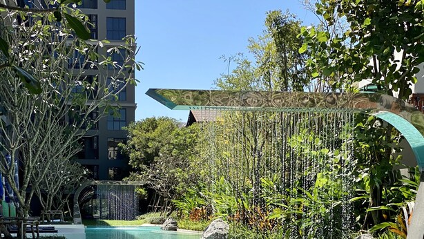 A swimming pool with a waterfall feature, surrounded by lush greenery and modern architecture.