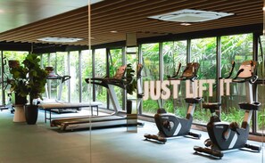 Un gimnasio con equipo de ejercicio, ventanas amplias y plantas de interior.