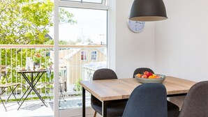 A modern dining area with a wooden table, grey chairs, a black pendant light, and a bowl of fruit.