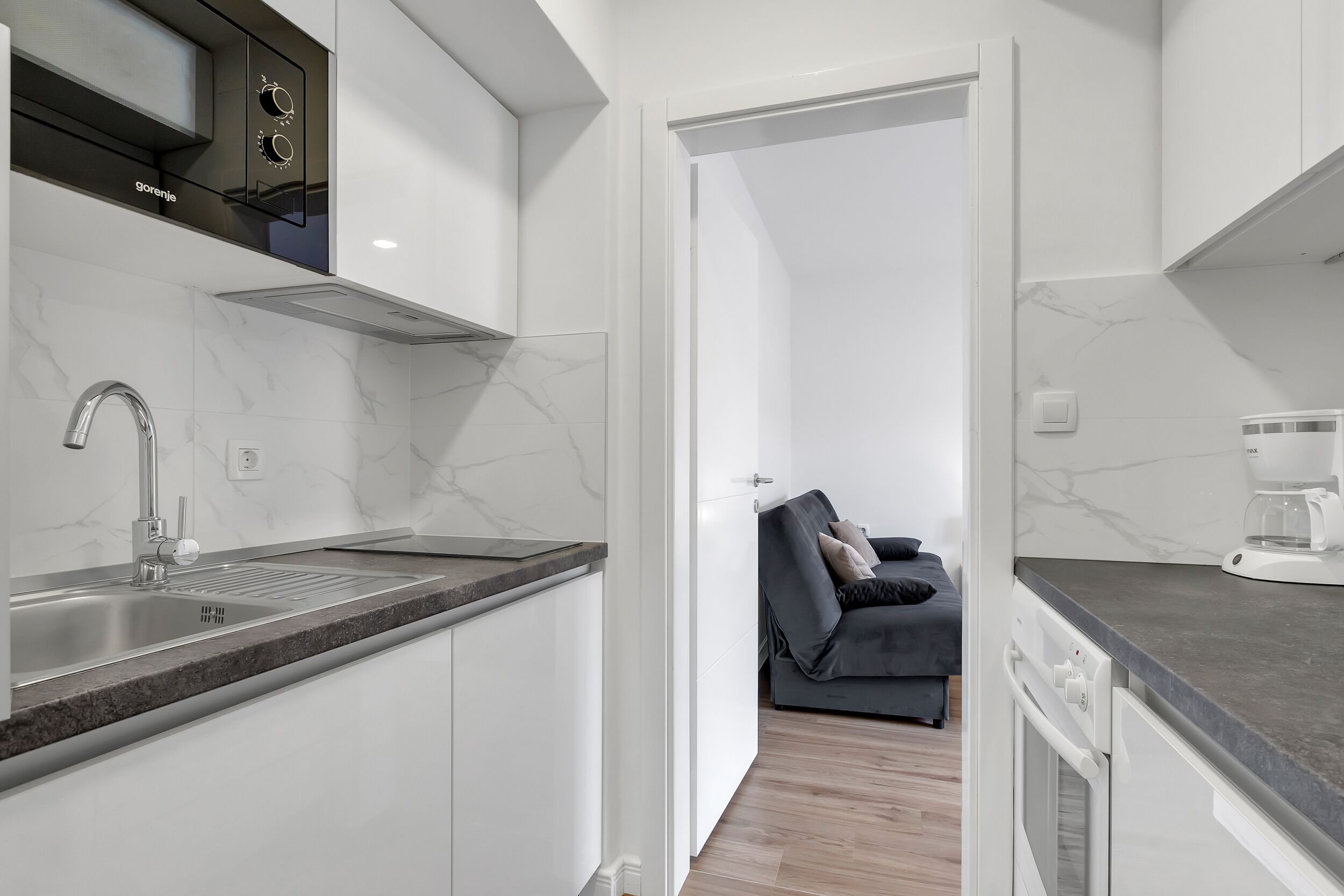 A modern kitchen with a built-in oven, a sink, and a coffee maker.