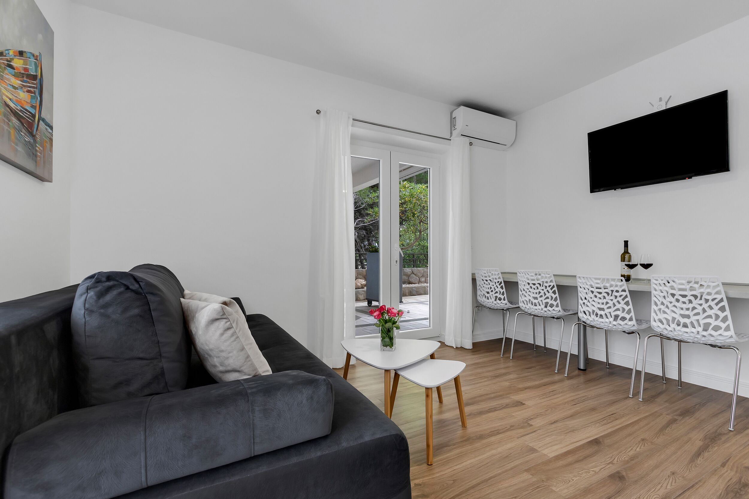 Un salon moderne avec un canapé gris, une table basse blanche et un téléviseur fixé au mur.