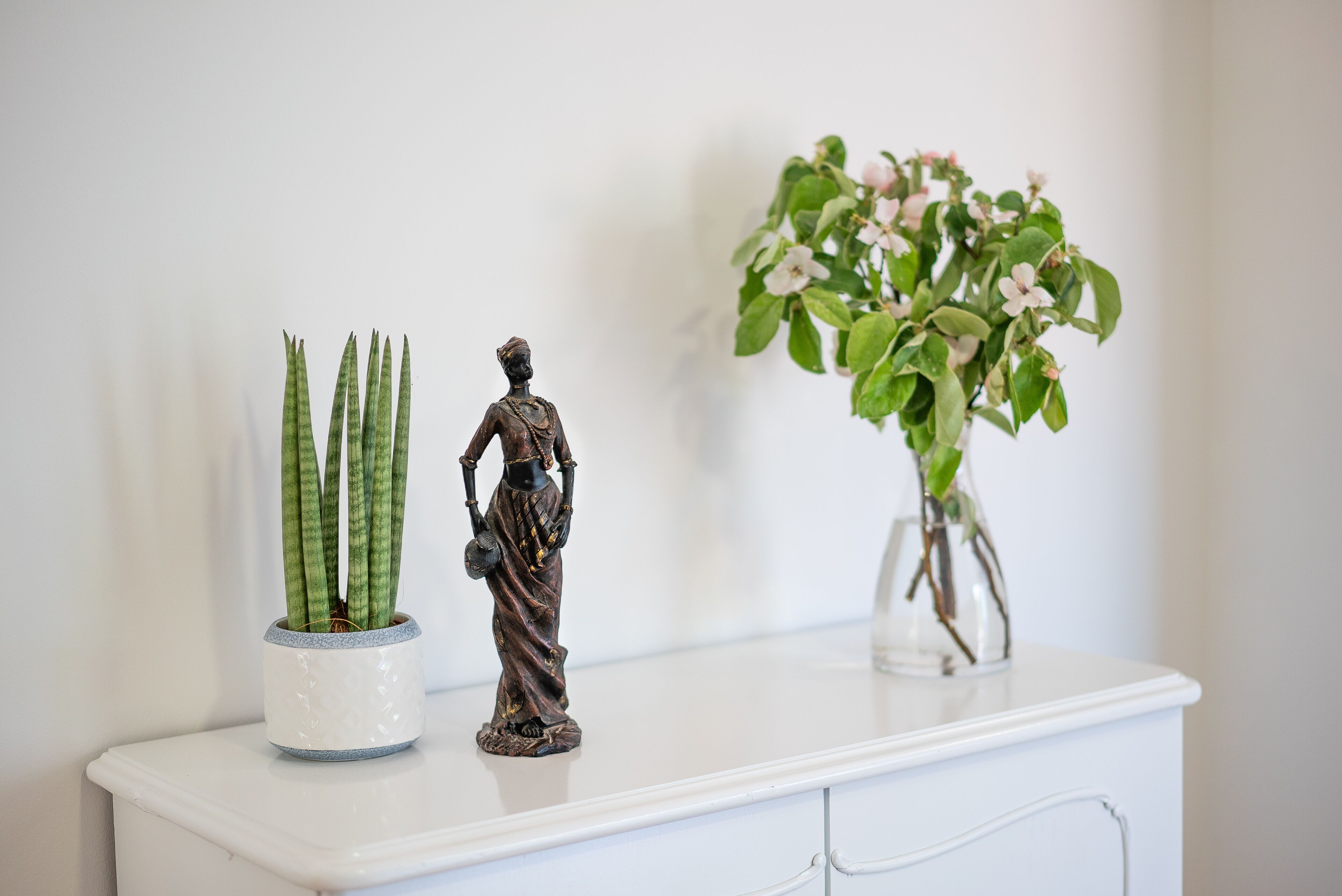 Een witte kast met een beeld en twee planten in potten.