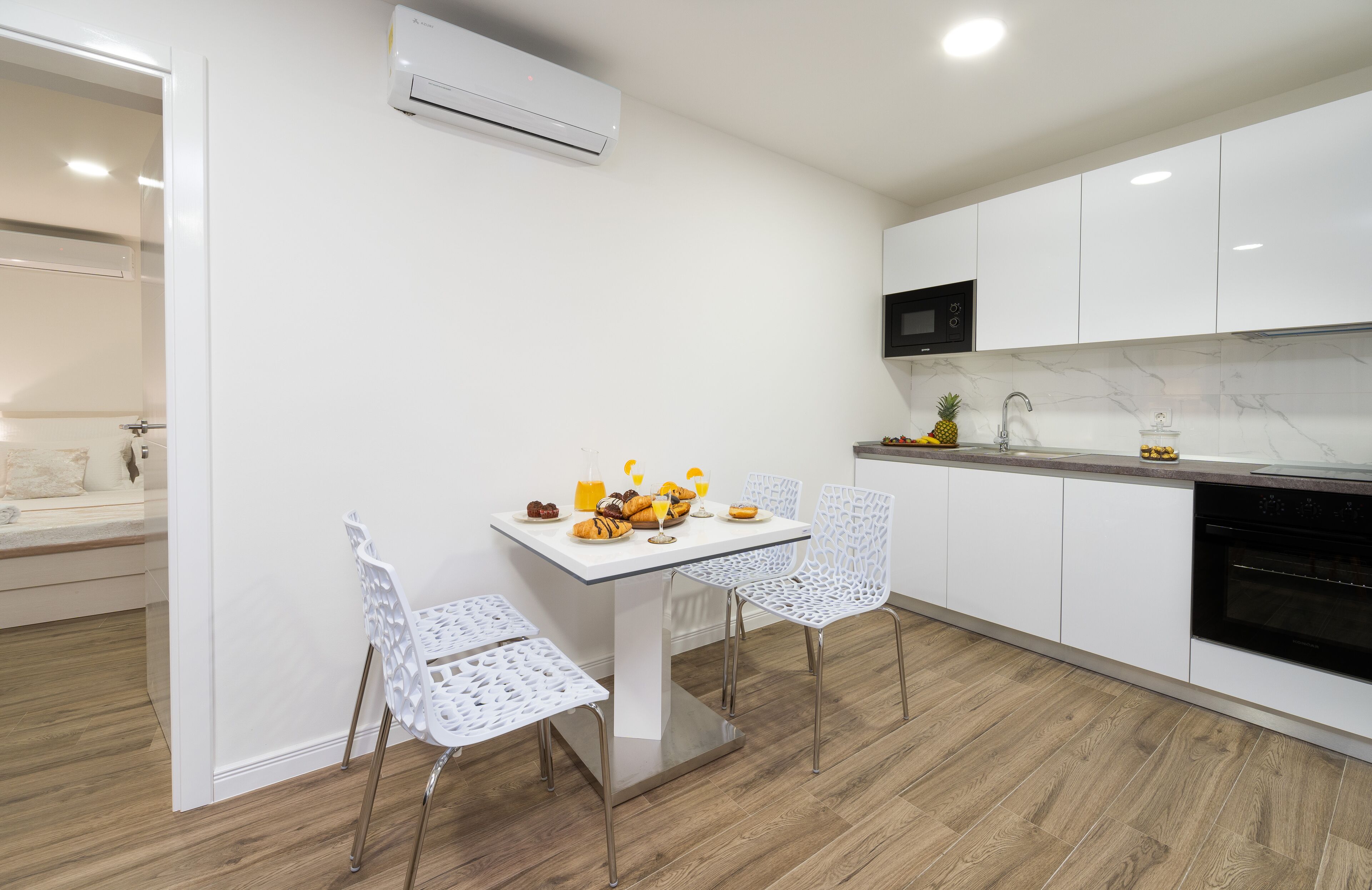 A modern kitchen with white cabinetry, a built-in oven, and a dining area with a white table and chairs.