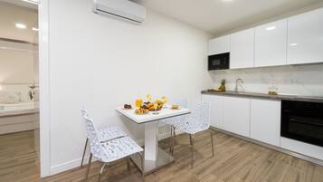 A modern kitchen with white cabinetry, a built-in oven, and a dining area with a white table and chairs.