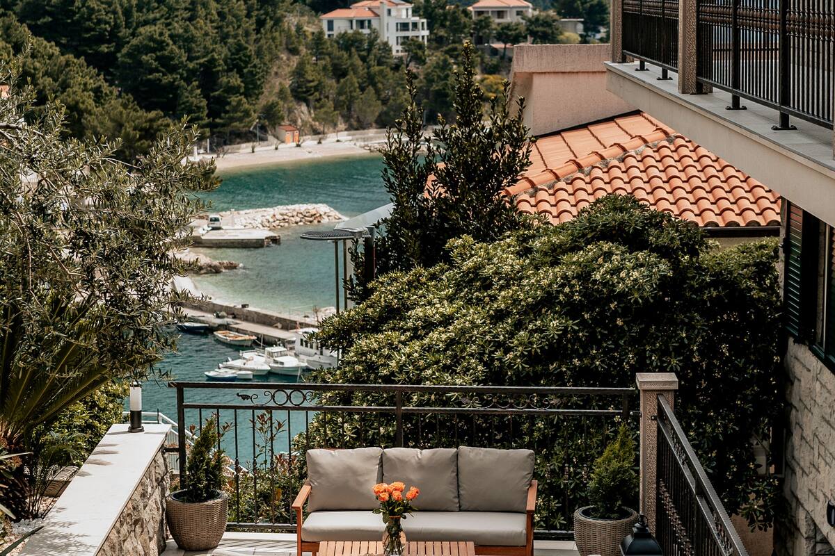 Un balcon avec un canapé et des fauteuils, donnant sur une zone côtière avec une plage et des montagnes.