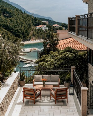 Un balcón con sofá y sillones, con vistas a una zona costera con playa y montañas.