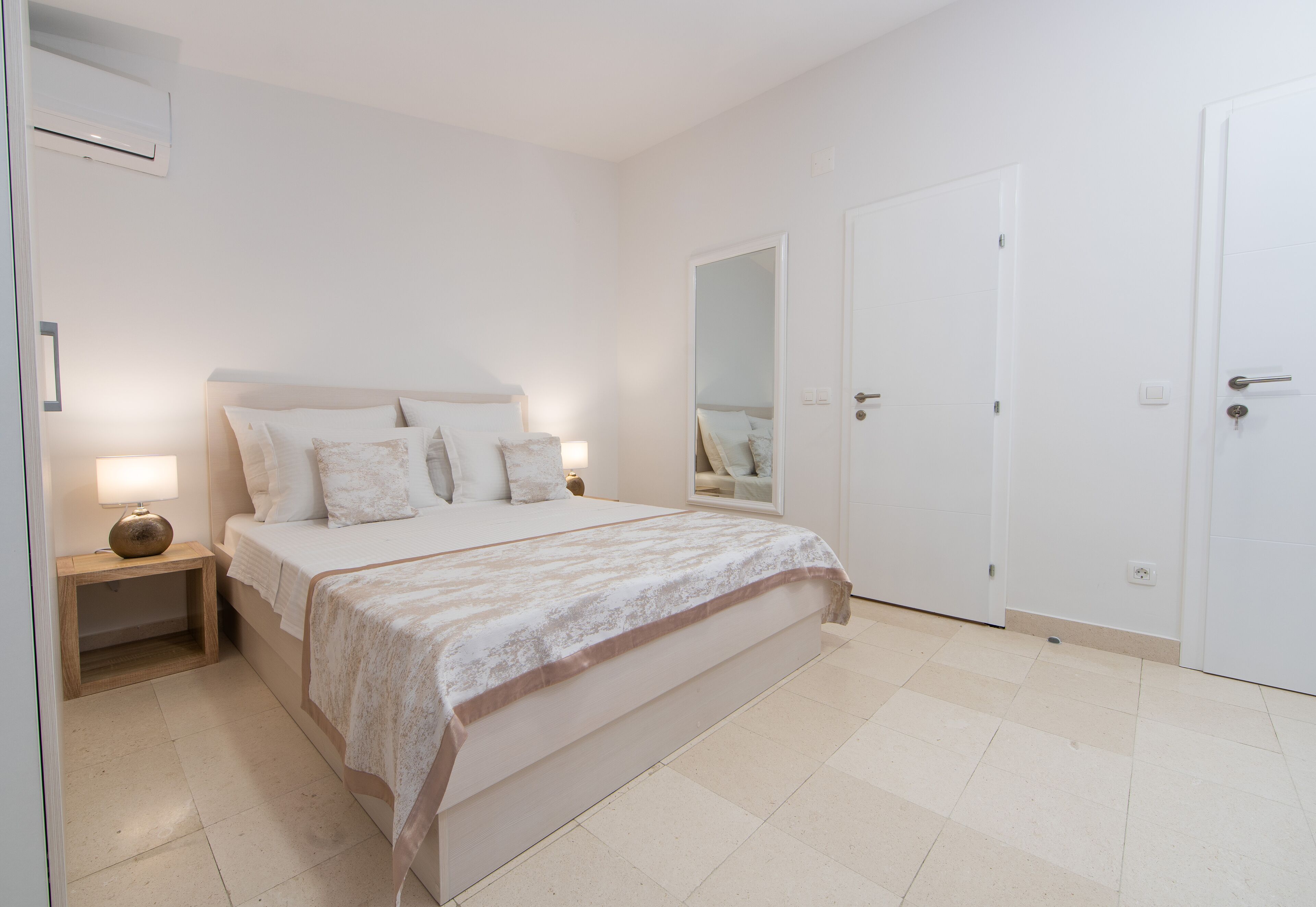 Un dormitorio con cama, lámparas de noche, mesita de noche, espejo y puerta.