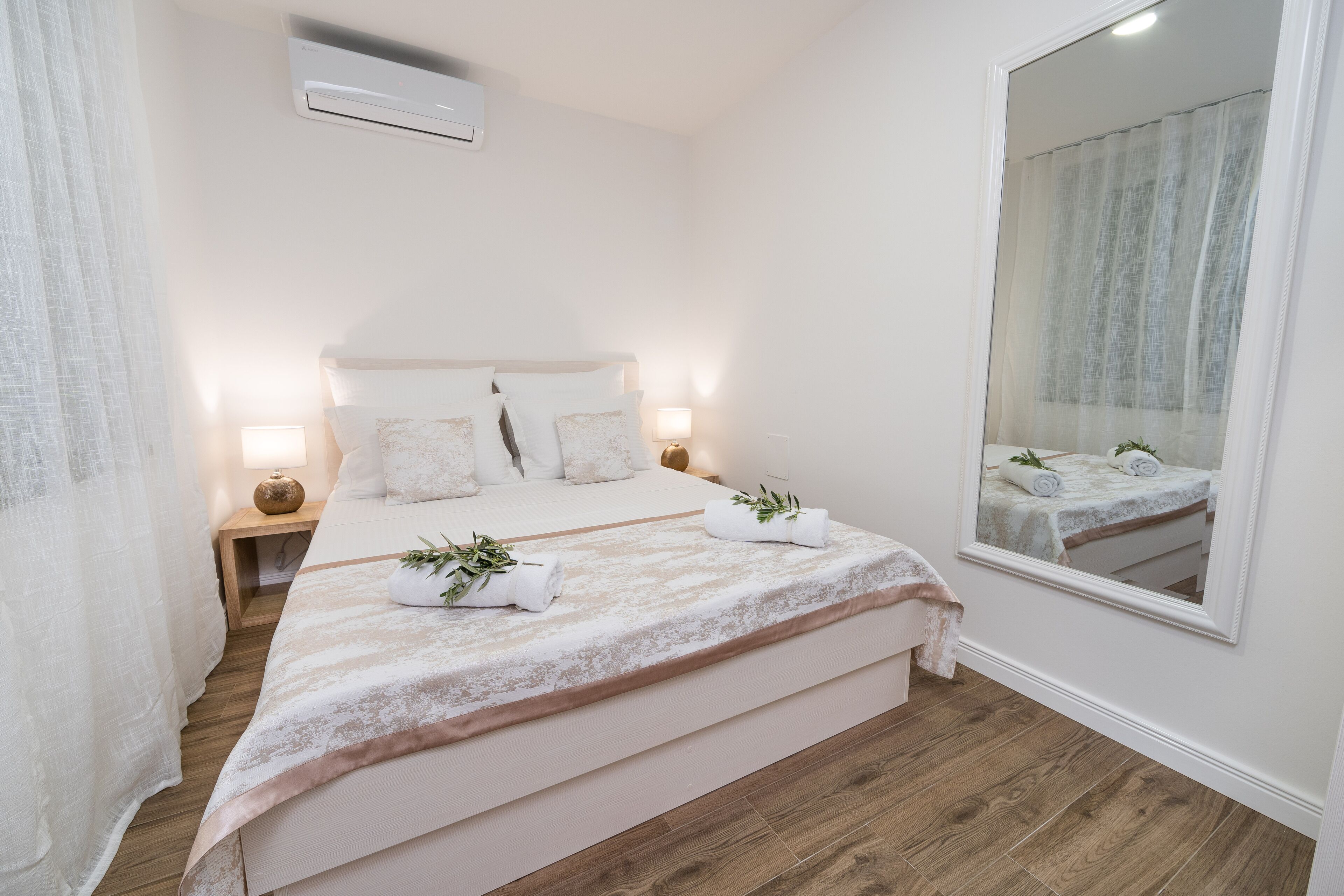 Un dormitorio ordenado con una cama grande, lámparas de noche, un espejo y suelo de madera.
