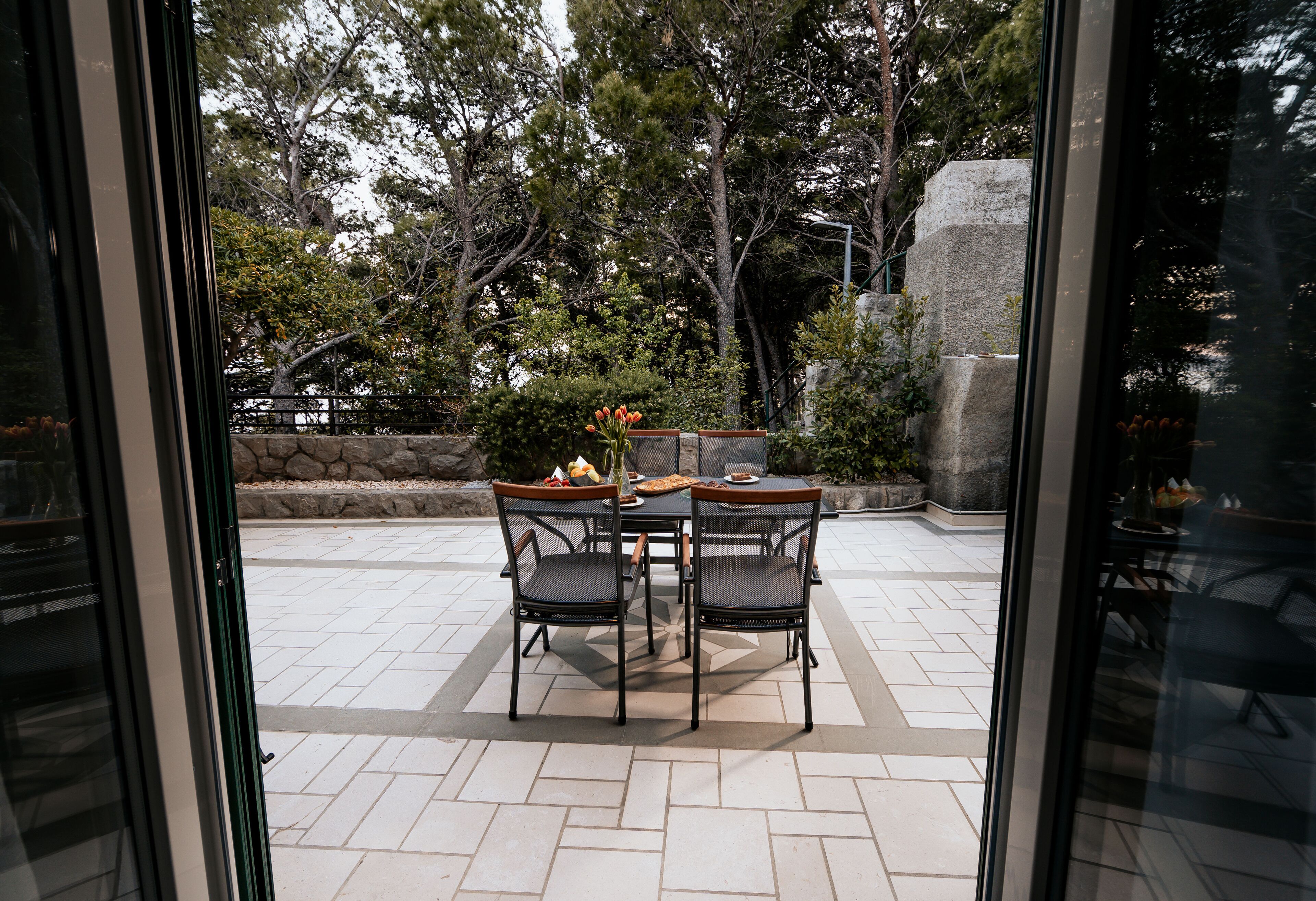 Un patio al aire libre con una mesa y sillas, rodeado de muros de piedra y árboles.