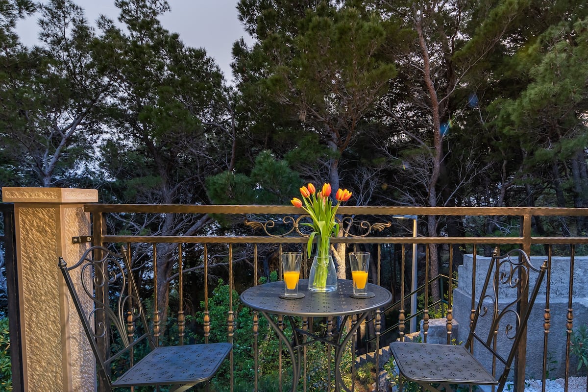 Un balcon avec une table ronde, deux chaises et un vase rempli de fleurs.