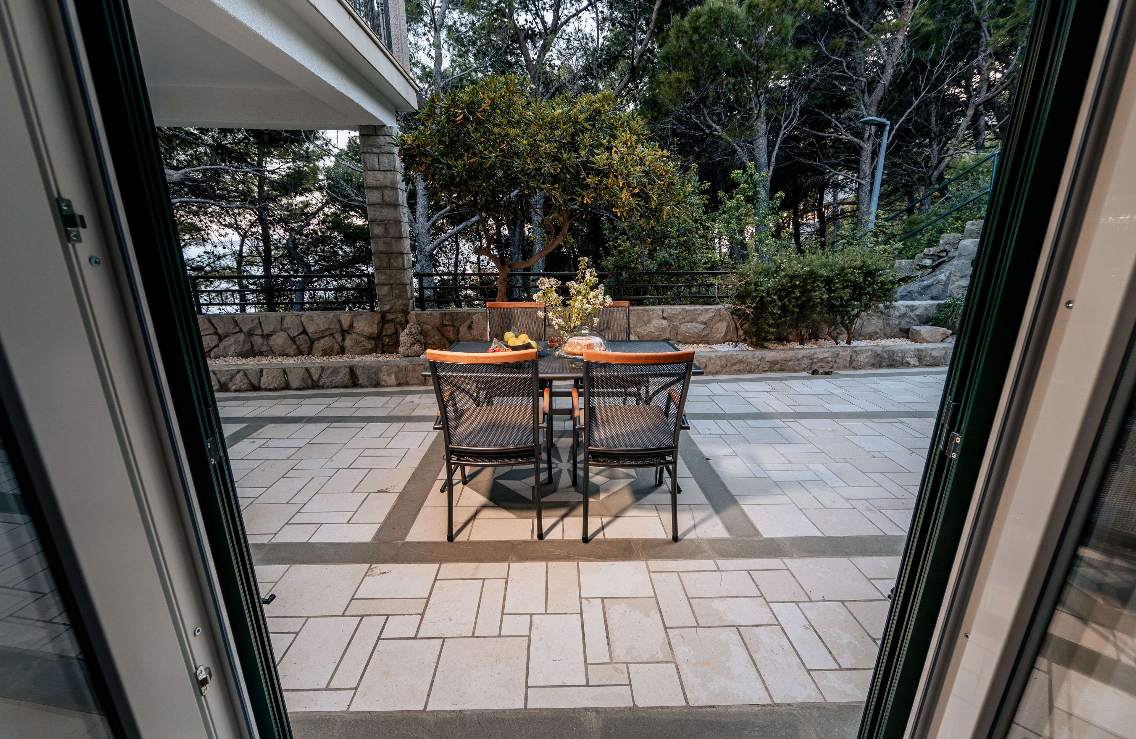 Une terrasse extérieure avec une table et des chaises, entourée de murs en pierre et d’arbres.