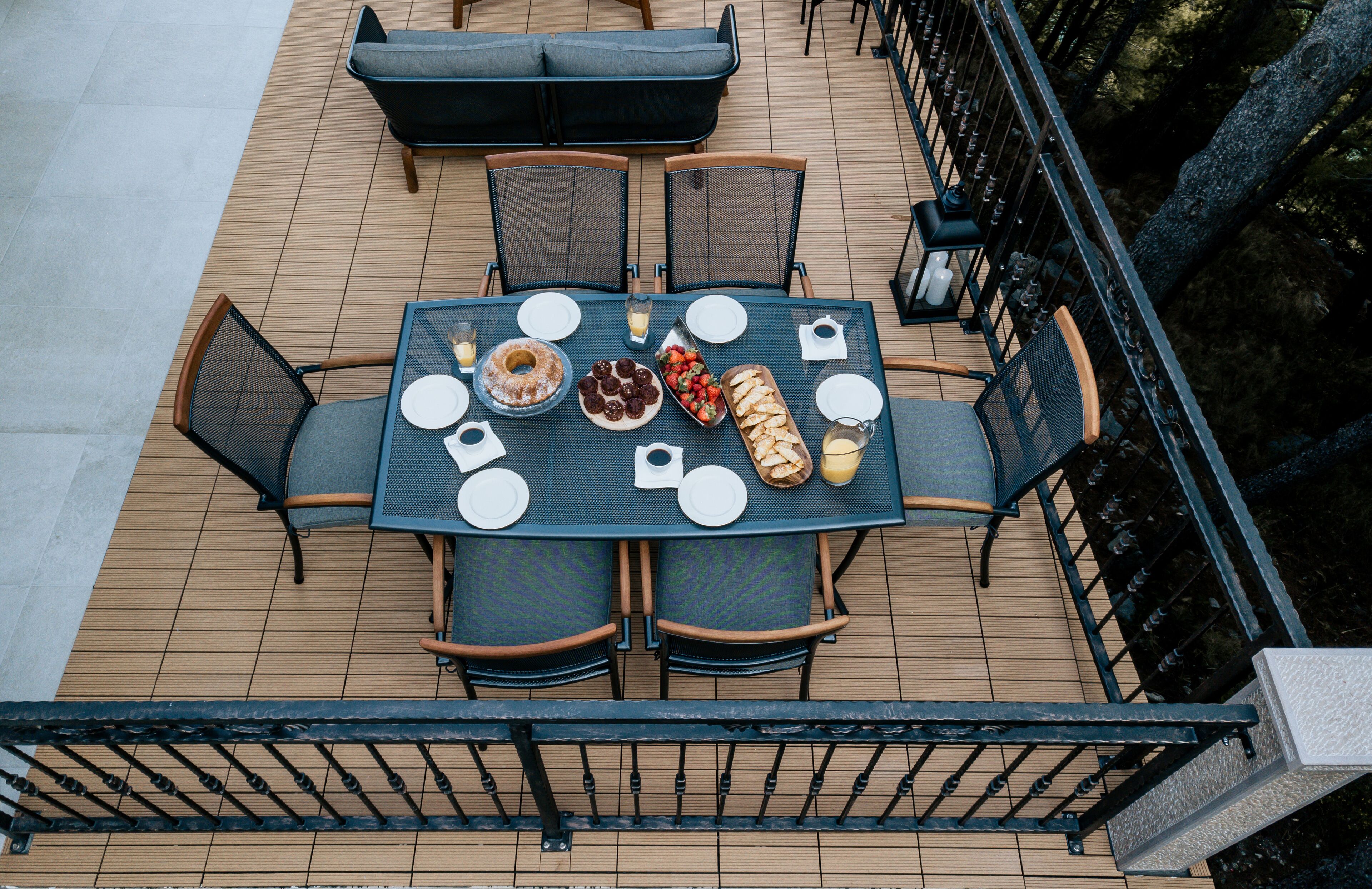 A rooftop terrace with a table set for dining, surrounded by chairs and a sofa.