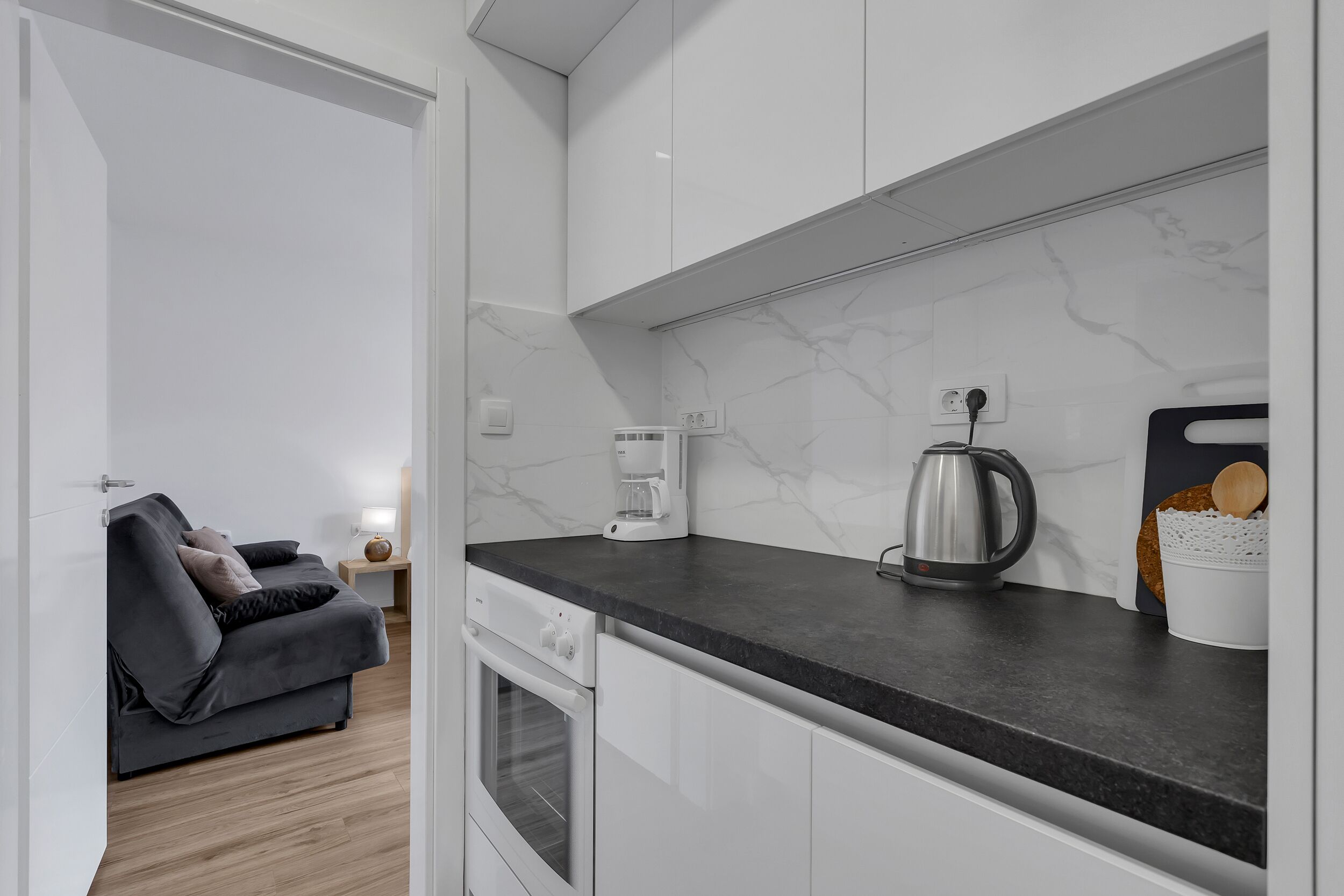 A modern kitchen with white cabinets, a black countertop, and a coffee maker.
