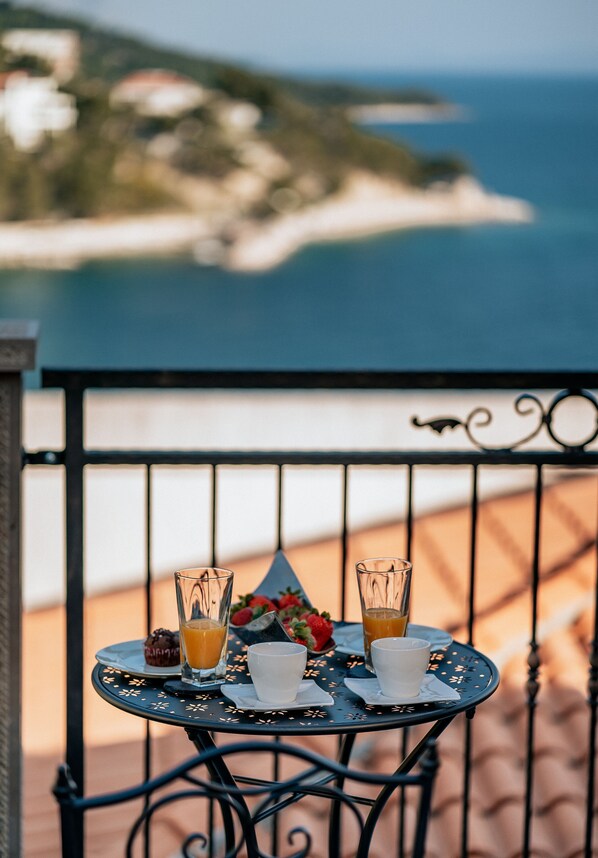 Una mesa con dos vasos de jugo de naranja, una taza y un postre en un balcón con vistas al mar.