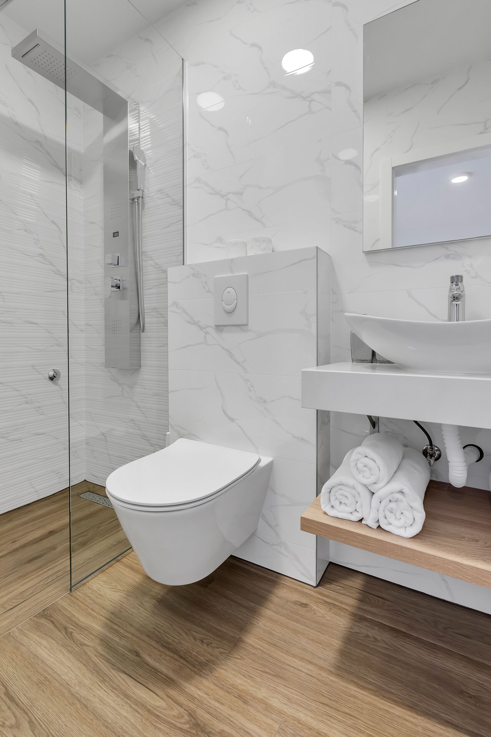 A modern bathroom with a glass shower enclosure, a white toilet, and a wooden vanity with a sink and towel rack.