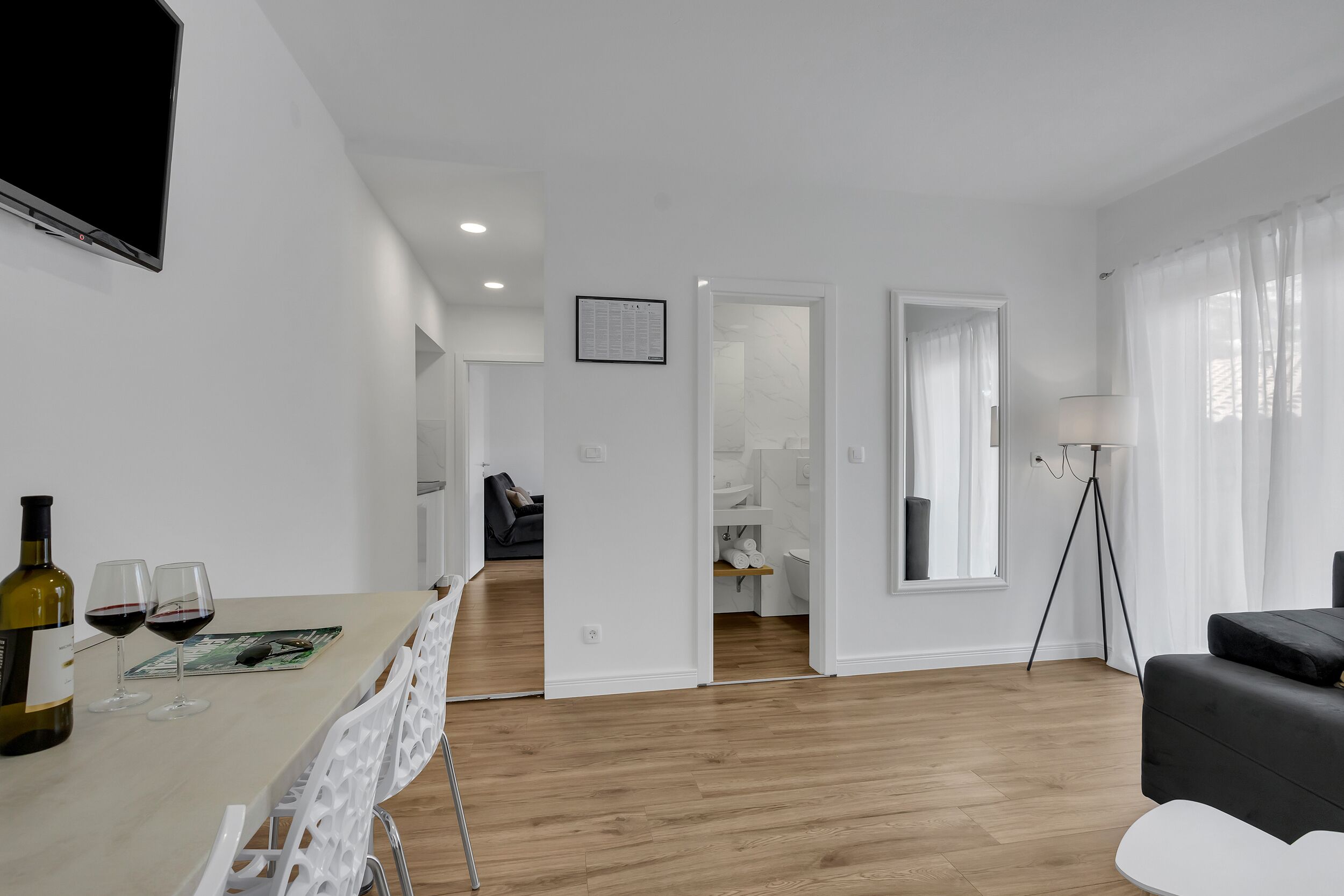 Uma sala de estar moderna com área de refeições, piso de madeira, um sofá e um abajur.
