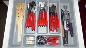 A drawer with various kitchen utensils including spoons, forks, knives, and a wooden spatula.