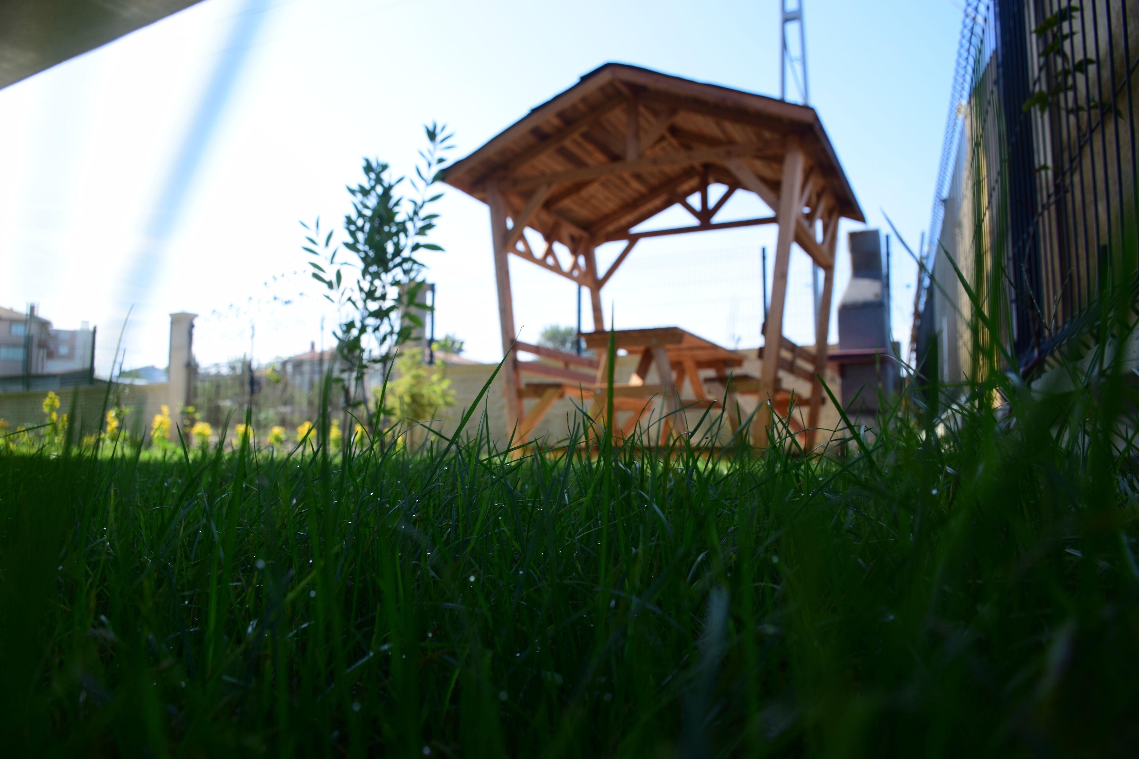 A wooden gazebo in a grassy area with a building in the background.
