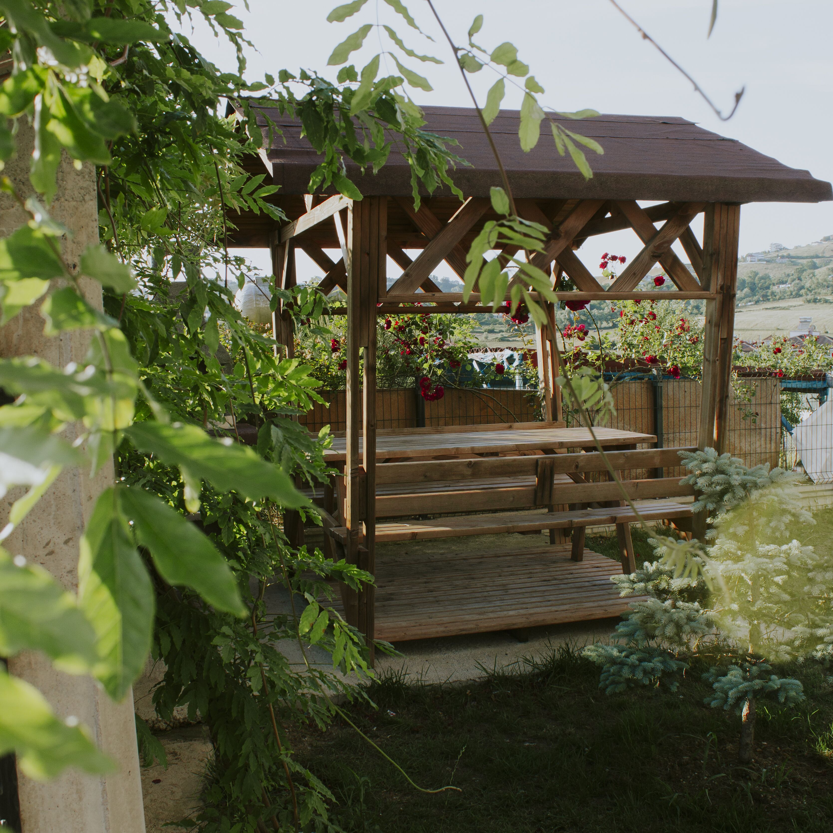 A wooden gazebo with steps, surrounded by lush greenery and flowering plants.