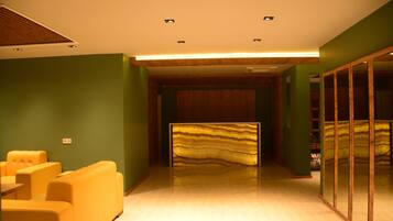 A modern hotel lobby with a reception desk, seating area, and a large mirror.