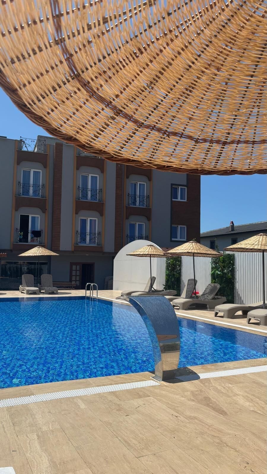 Piscina con sillones de playa y sombrillas, rodeada por un edificio con balcones.
