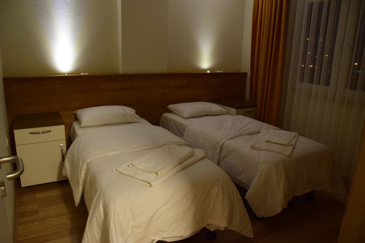 A hotel room with two beds, a wooden headboard, a nightstand, and a window with curtains.