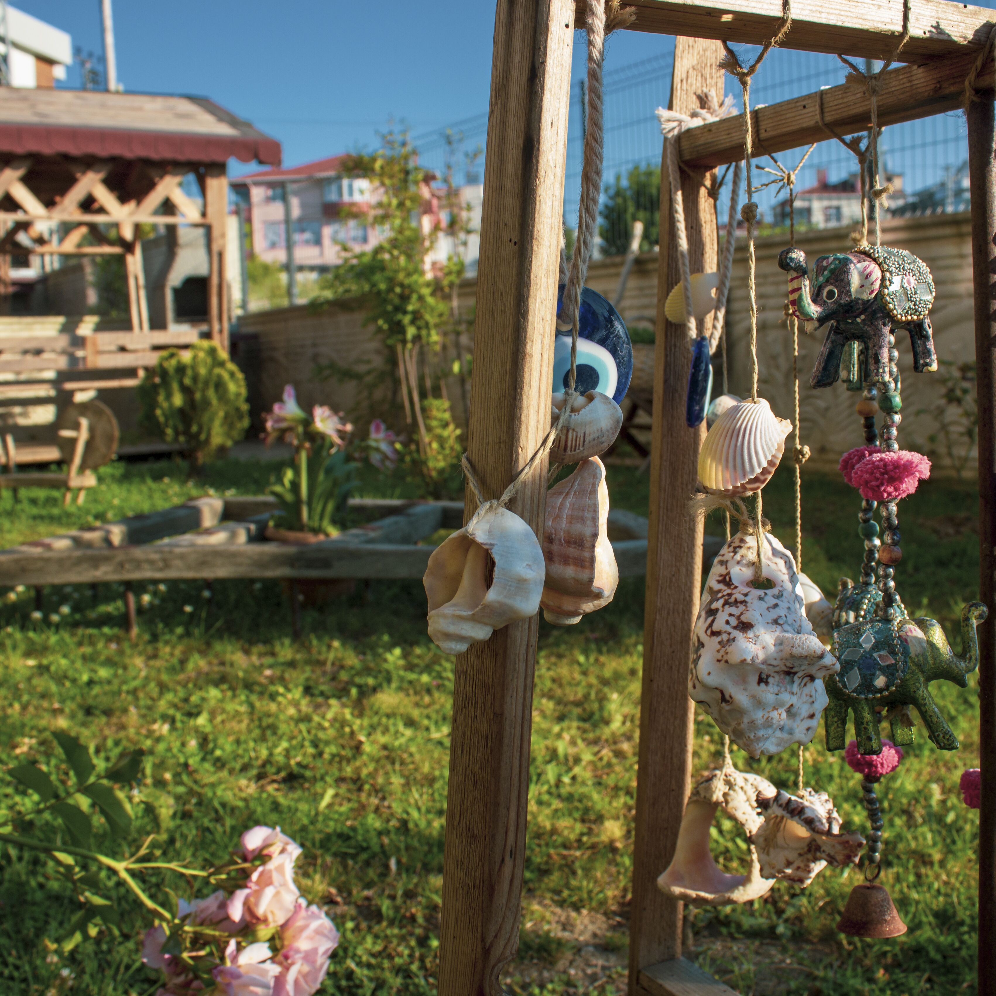 A wooden structure with hanging decorative items, including seashells and a toy elephant, in a garden setting.