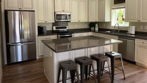 A modern kitchen with white cabinetry, stainless steel appliances, a large island with stools, and a window with a view of the outdoors. - Incredibly spacious Gathering place, Private Pickleball Court, Sleeps 14, (Scottsdale)