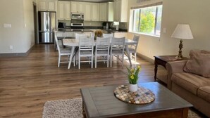 A spacious living area with a dining table and chairs, a coffee table with a decorative coaster, a sofa, and a kitchen in the background. - Incredibly spacious Gathering place, Private Pickleball Court, Sleeps 14, (Scottsdale)