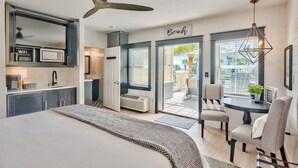 A modern bedroom with a large bed, a ceiling fan, a kitchenette, and a view of the beach. - Beach Views on 30A! (Santa Rosa Beach)