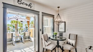 A modern room with a dining area featuring a round table and four chairs, a ceiling light fixture, and a view of the outdoor patio with umbrellas and chairs. - Beach Views on 30A! (Santa Rosa Beach)