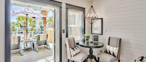 A modern room with a dining area featuring a round table and four chairs, a ceiling light fixture, and a view of the outdoor patio with umbrellas and chairs.