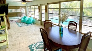Un comedor con una mesa redonda y sillas, una alfombra estampada y ventanas amplias que dan a una piscina.