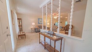 Un pasillo con una consola de madera, una mesa con superficie de vidrio y un espejo grande con marco decorativo.