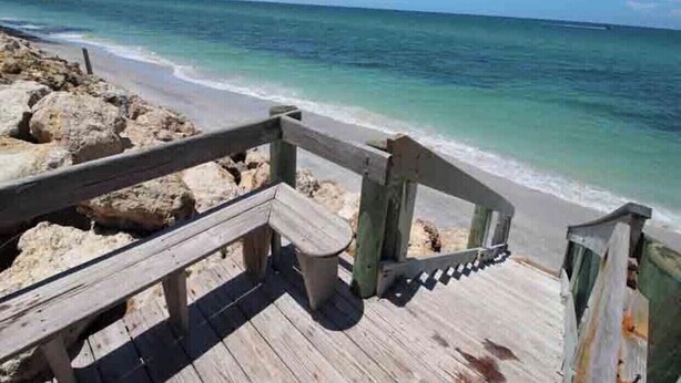 Un paseo marítimo de madera que conduce a una playa con aguas turquesas cristalinas.