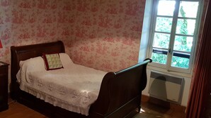 Una camera da letto con un letto di legno, un comodino con una lampada, carta da parati floreale e una finestra vista su spazi verdi.