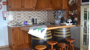 Une cuisine avec des meubles en bois, un dosseret carrelé, une cuisinière à gaz et un coin bar avec des tabourets.
