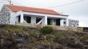 Une maison située sur la côte, avec une façade blanche, un toit recouvert de tuiles rouges et une clôture en bois.