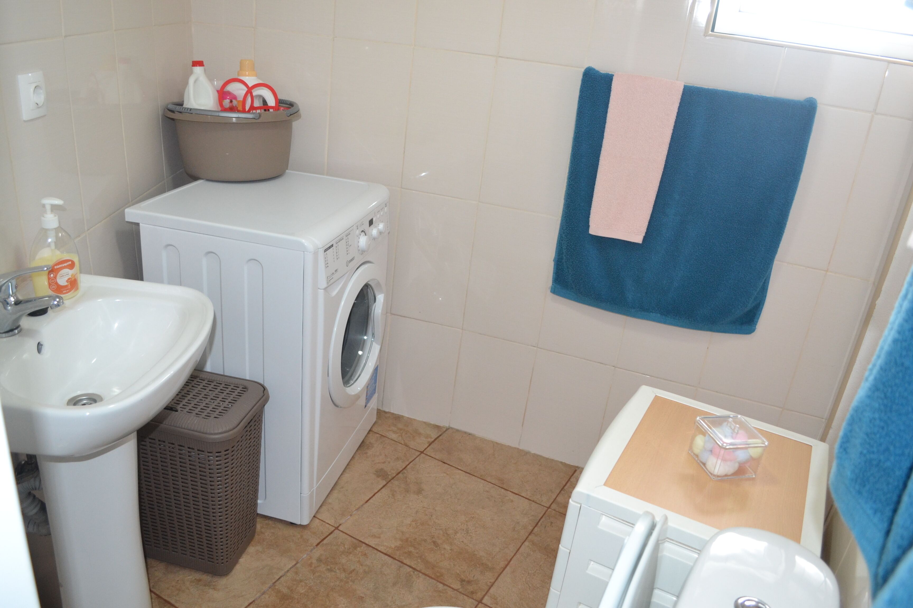 A compact bathroom with a sink, washing machine, and a towel rack.