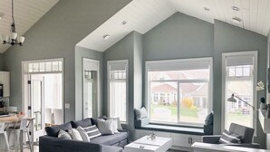 A spacious living room with a grey sofa, a white coffee table, and a large window offering a view of the outside.