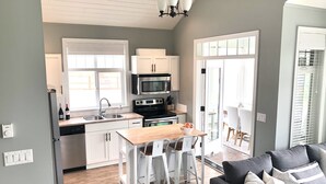 A modern kitchen with white cabinets, a central island, and a dining area with a gray sofa.