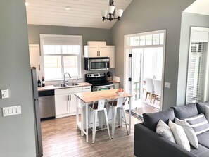 A modern kitchen with white cabinets, a central island, and a dining area with a gray sofa.